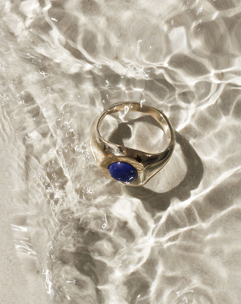 Gold stone set ring with lapis in centre on textured background